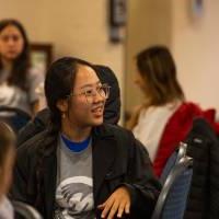 Students sitting at round tables listening to a speaker